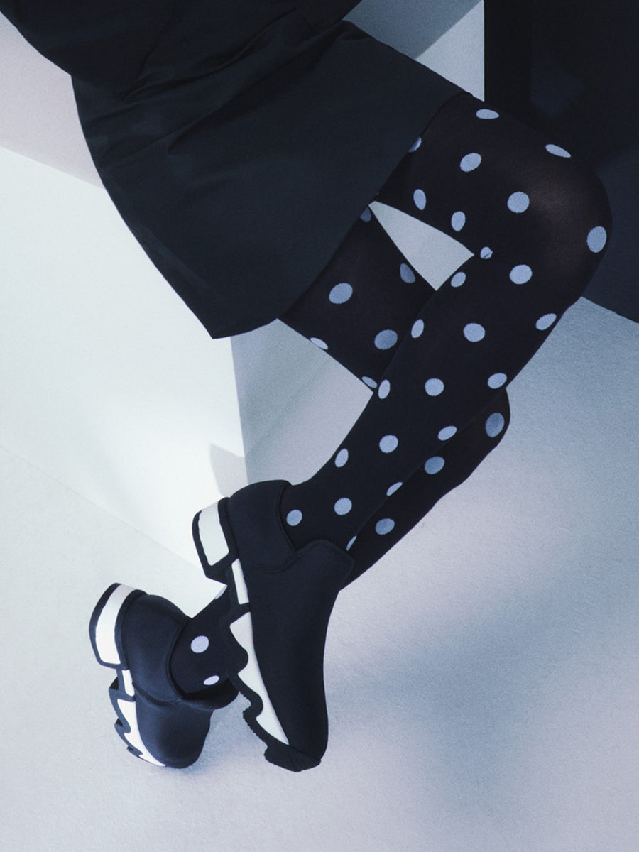 A model wearing iRi WES Black Outline Neoprene Low Top Sneaker with black & white polka dot tights