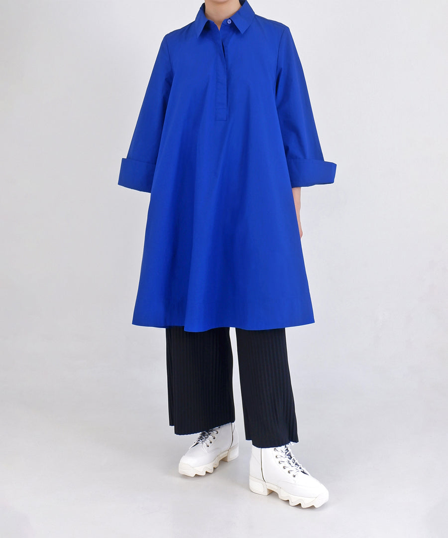 A model wearing AROM White Lace-Up Boot with black peated pants and oversized yves blue knee-length shirtdress